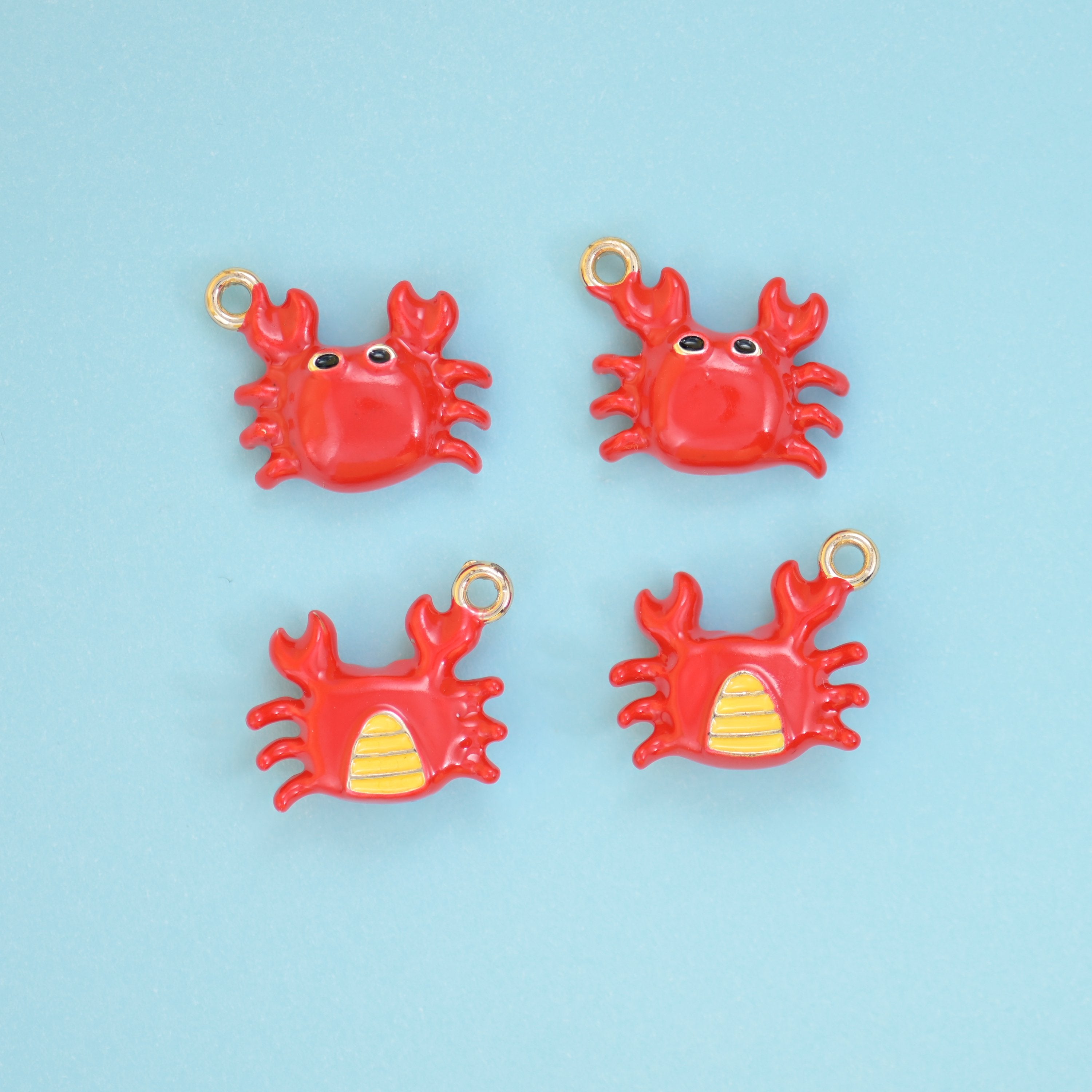 Enamel crab charms in red, front view with black eyes and reverse view showing the yellow striped belly