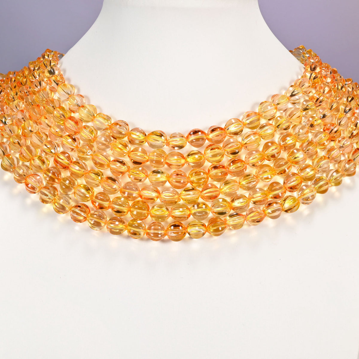 Yellow gold pumpkin glass beads shown as layered strands on a white neck display form.