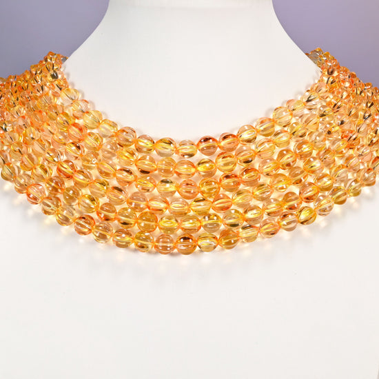 Yellow gold pumpkin glass beads shown as layered strands on a white neck display form.