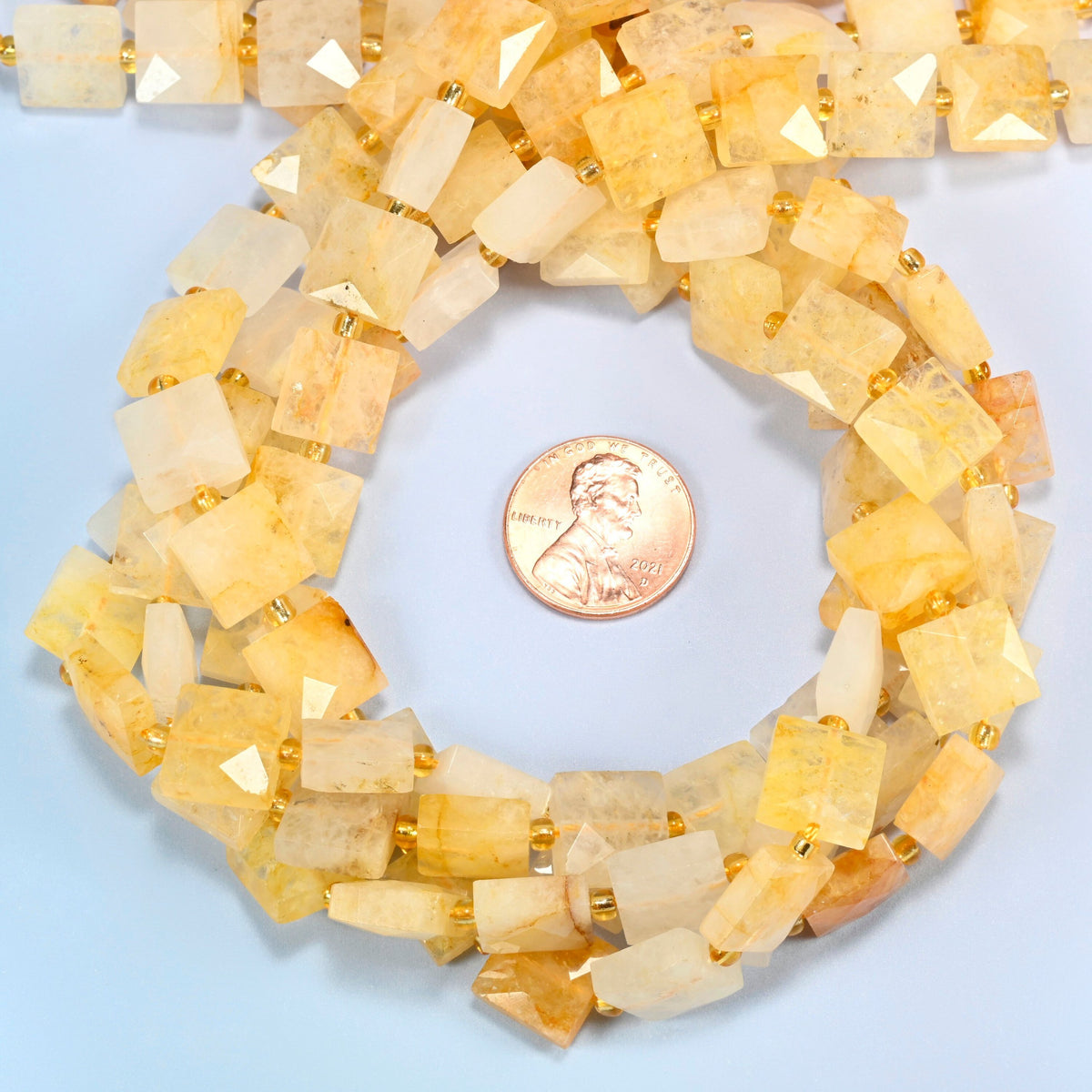 Natural golden healer quartz faceted flat square beads 10x10mm coiled in a loop around a US penny for scale, close-up of the faceted flat square shape