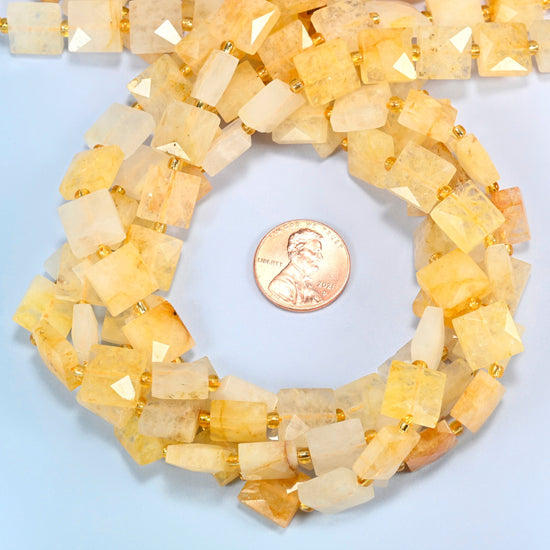 Natural golden healer quartz faceted flat square beads 10x10mm coiled in a loop around a US penny for scale, close-up of the faceted flat square shape