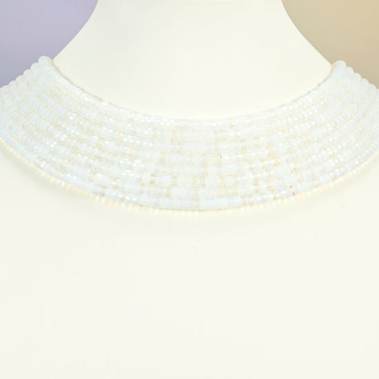 Opalite faceted heishi disc strands arranged as a layered collar on a white display bust, milky white beads across the neck