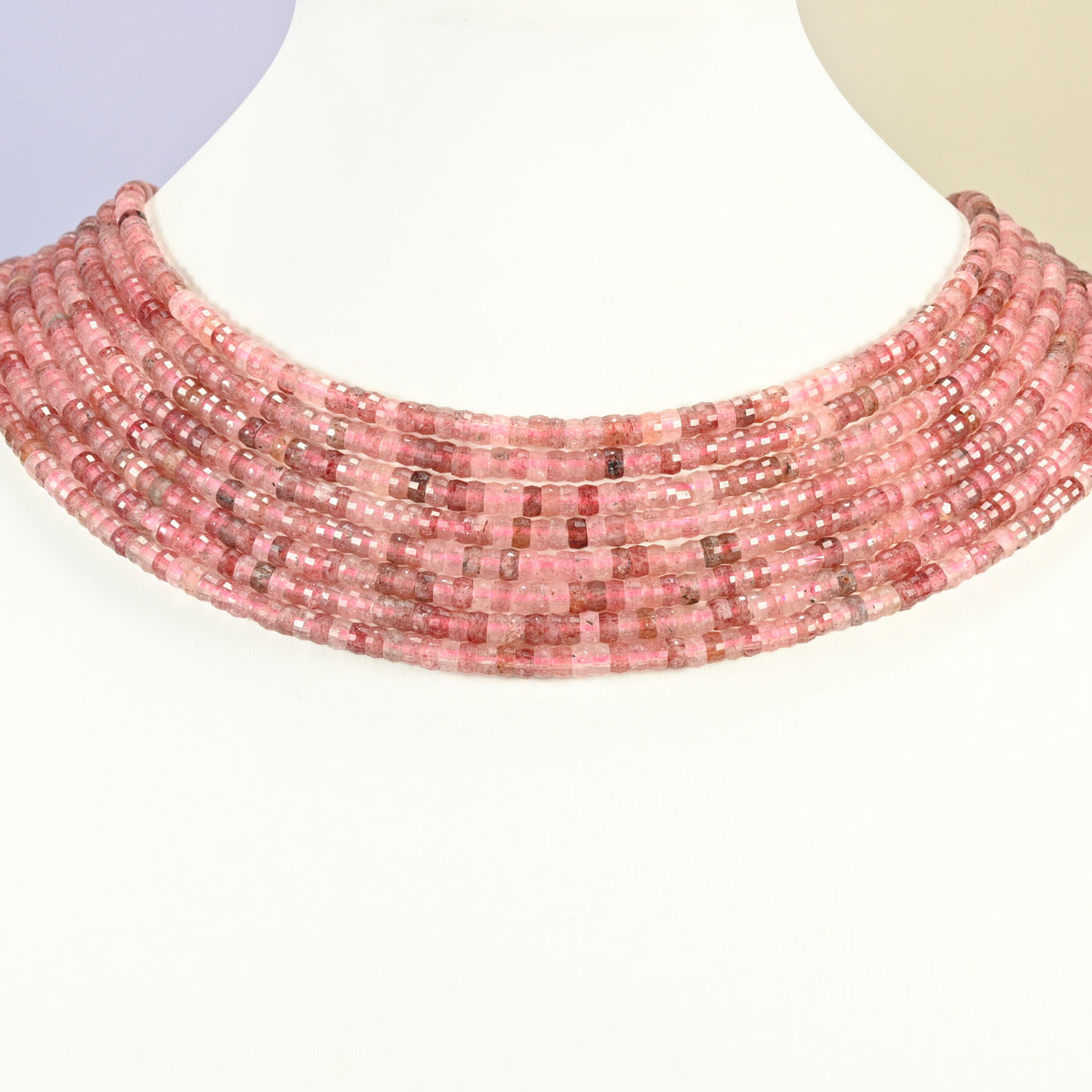 Strawberry quartz faceted heishi disc strands arranged as a layered collar on a white display bust, pink beads across the neck
