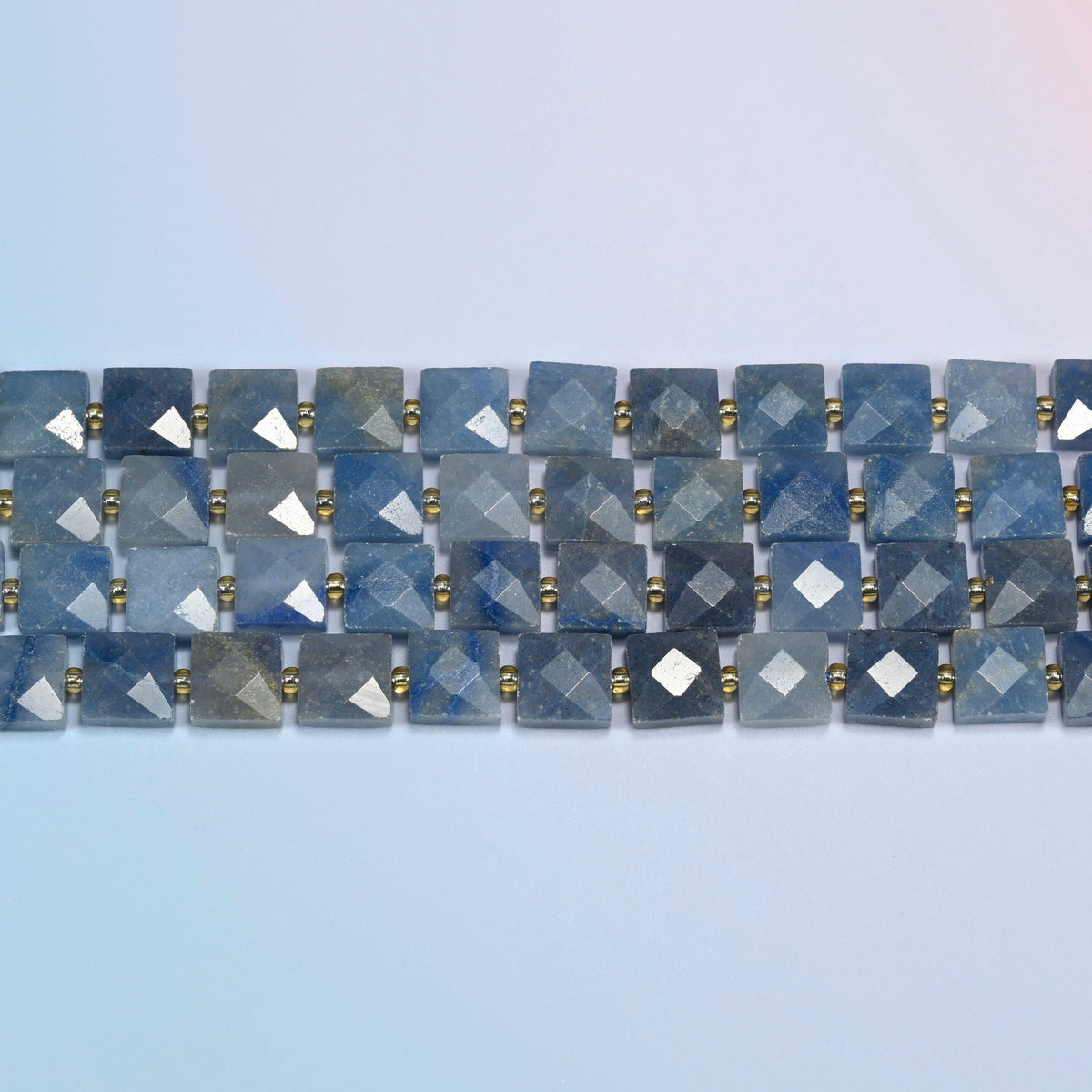 Several strands of natural blue aventurine faceted flat square beads laid in straight rows