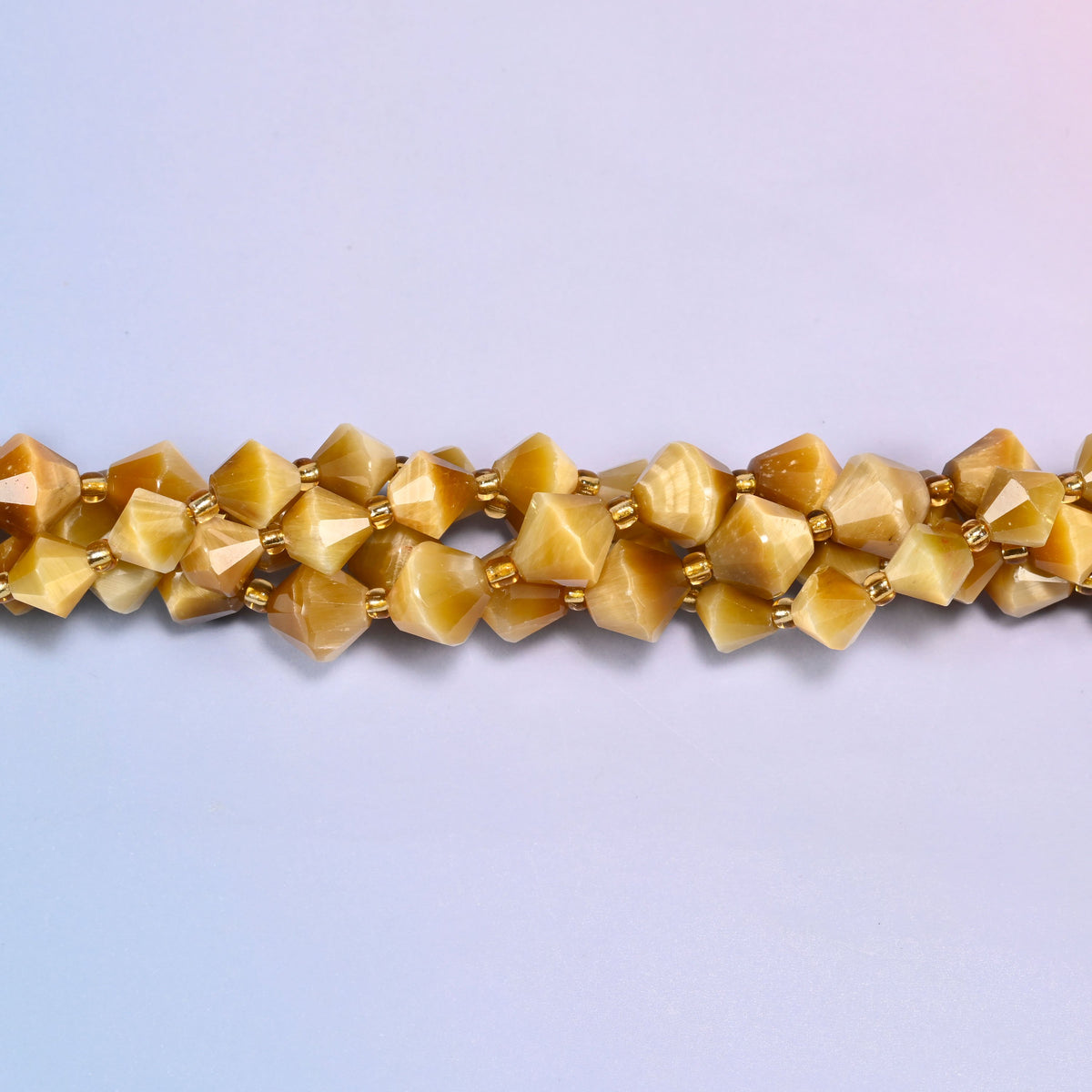Gold tiger eye bicone beads shown as a single strand laid straight across, warm brown and cream layers visible within single beads.