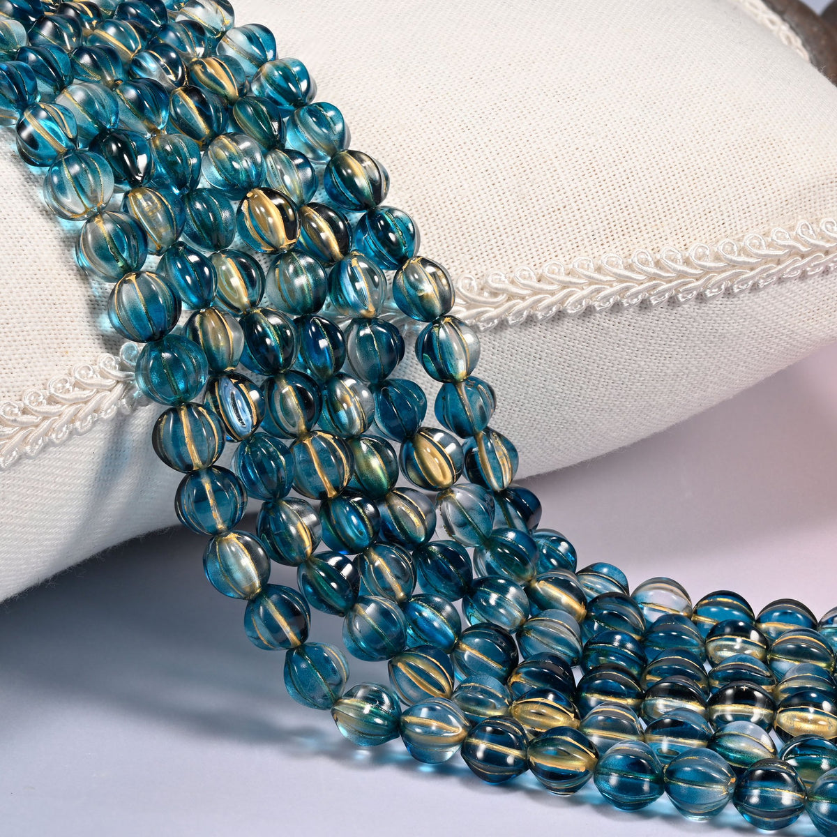 Dark blue gold pumpkin glass beads, 8mm fluted melon rounds, several strands draped over a white cushion.