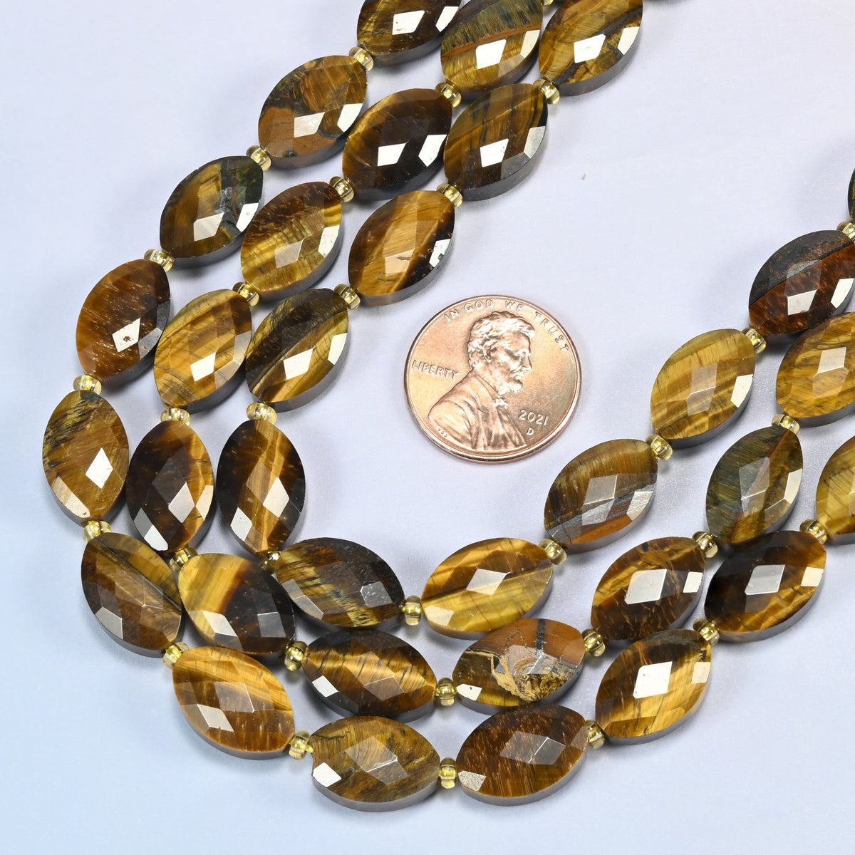 Close view of tiger eye faceted flat oval strands curving beside a US penny for scale