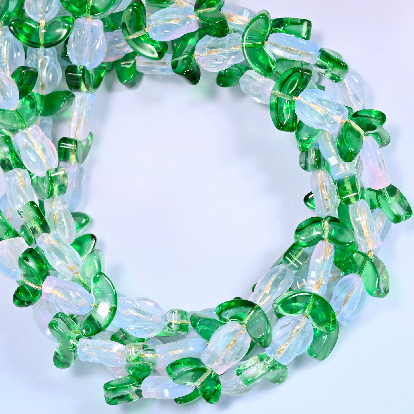Wide circular coil of white tulip and green leaf glass beads on a lavender and pink gradient background, showing the full wreath.