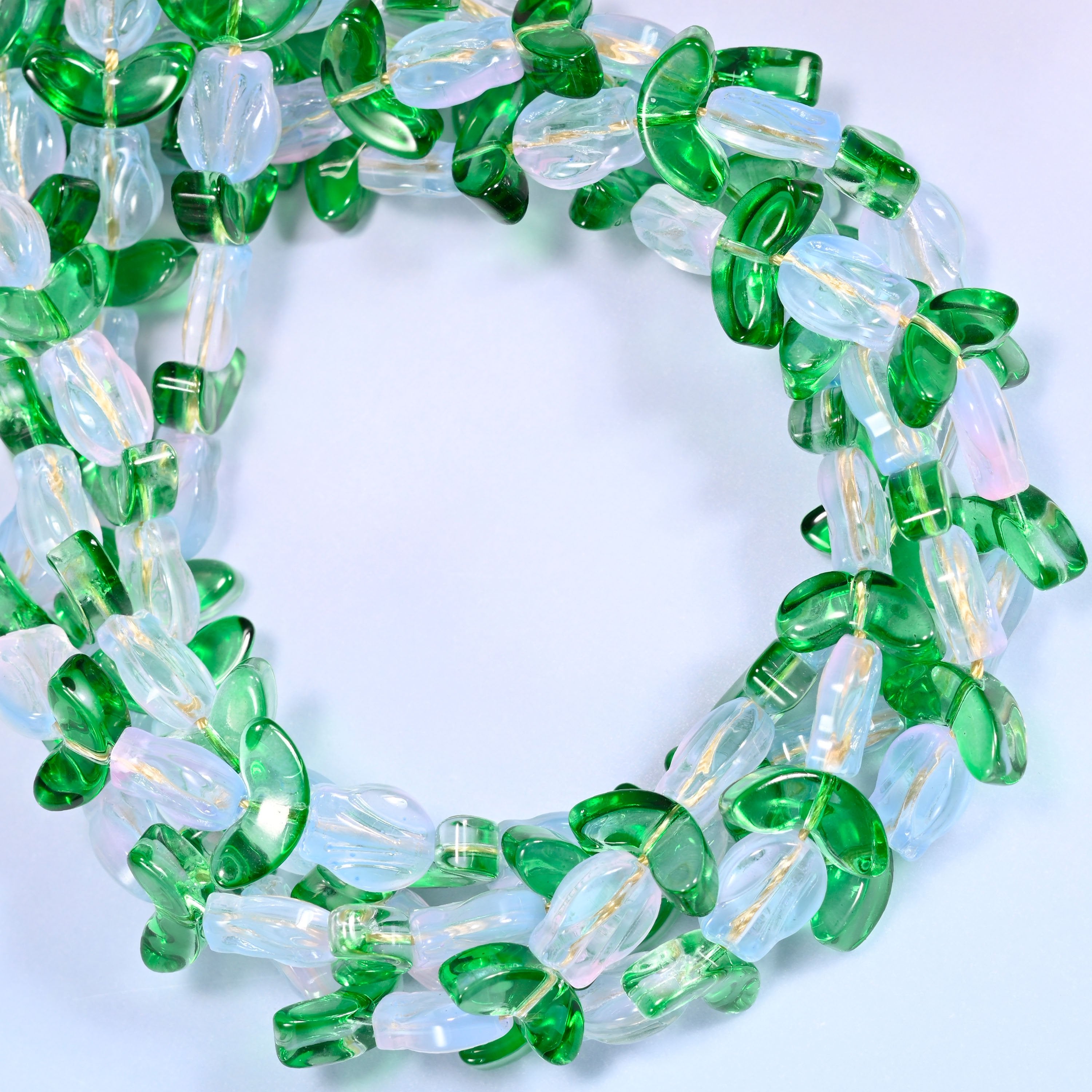 Wide circular coil of white tulip and green leaf glass beads on a lavender and pink gradient background, showing the full wreath.