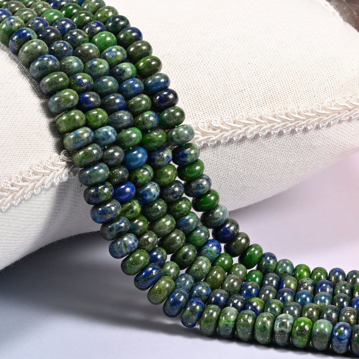 Close-up of multiple strands of polished Phoenix Lapis rondelle beads in blue and green tones with pyrite flecks, draped over a cream fabric jewelry display bust.