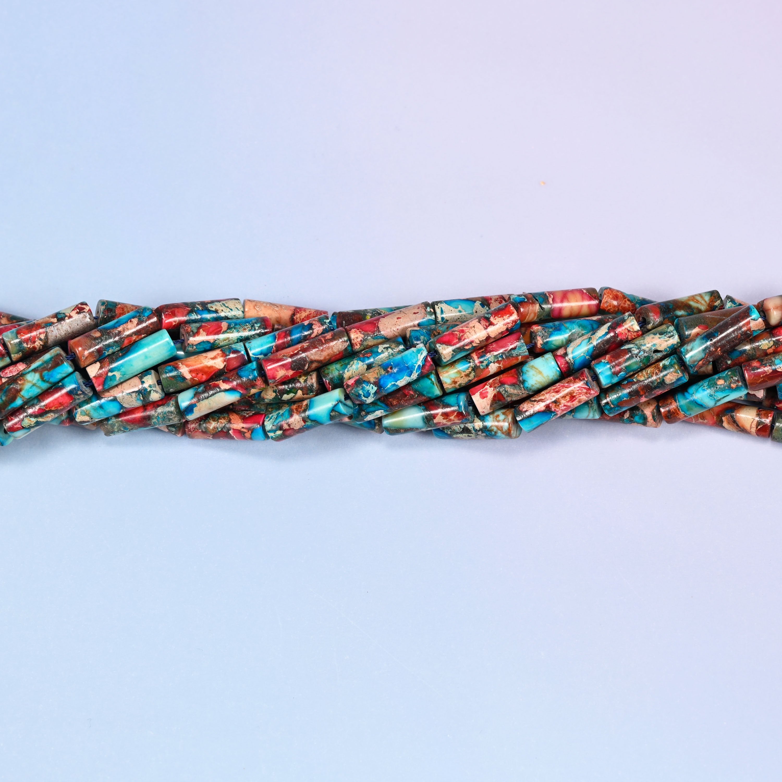 Close-up horizontal row of turquoise and coral jasper tube beads showing the twisted texture and color variation of the strand.