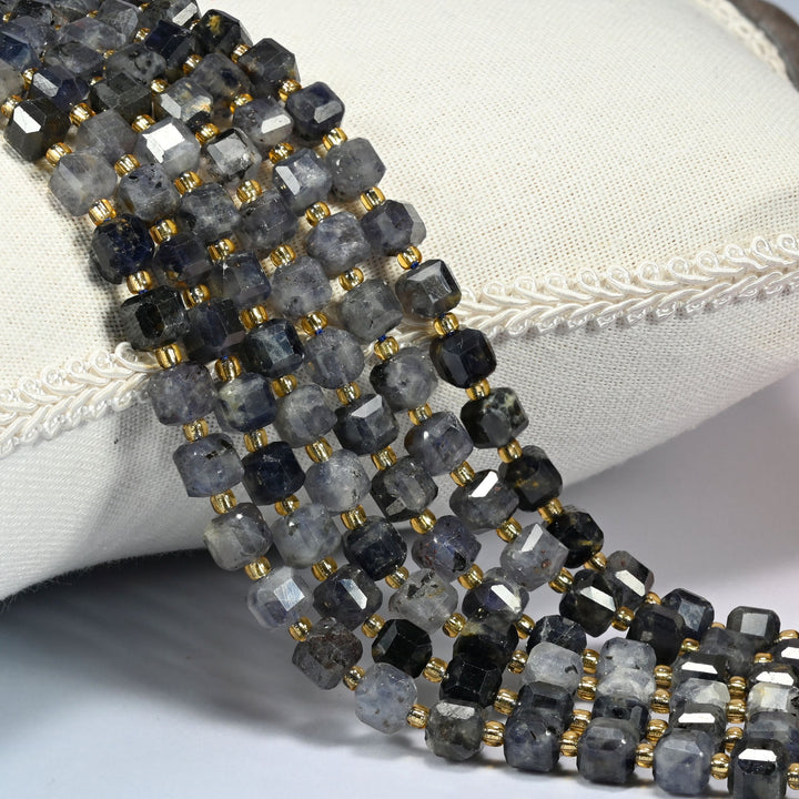 Iolite faceted cube beads 6mm with small gold spacer beads, several strands draped over a white cushion