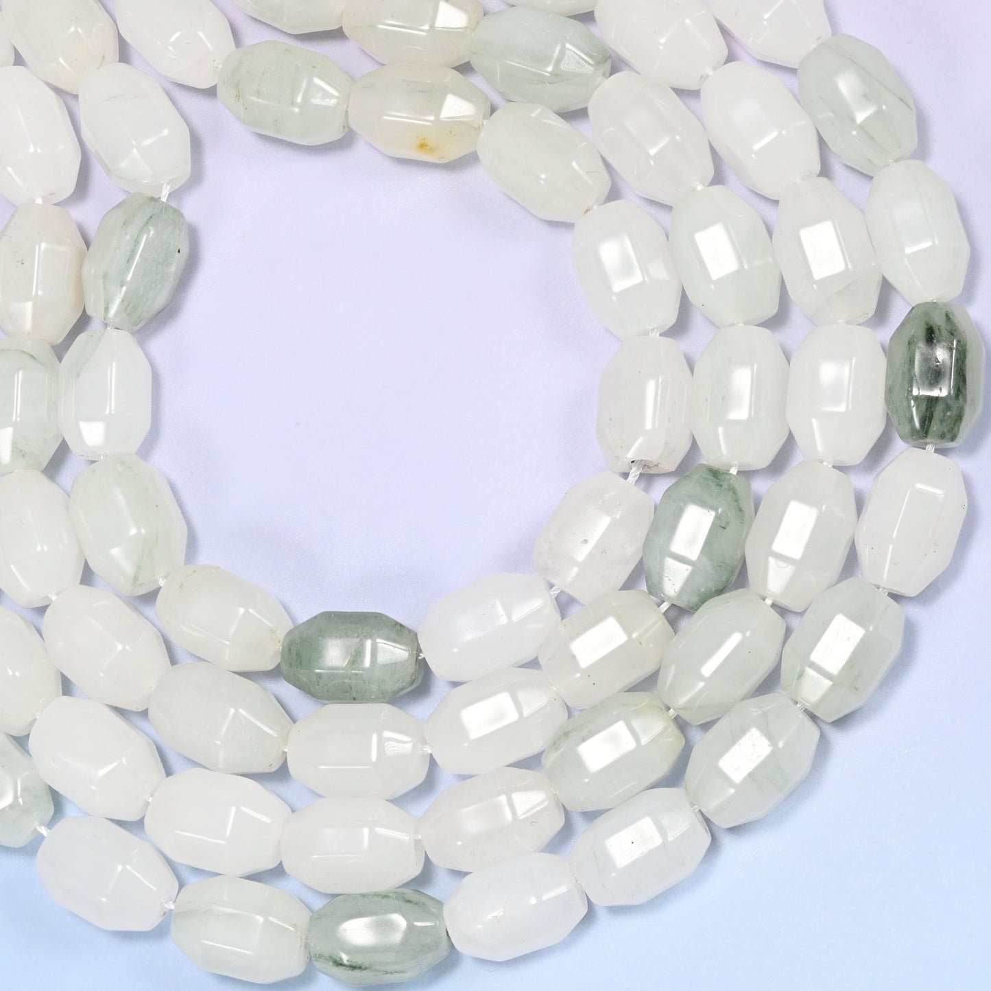 Close-up of a circular coil of Tianshan Jade faceted barrel beads on a light lavender background