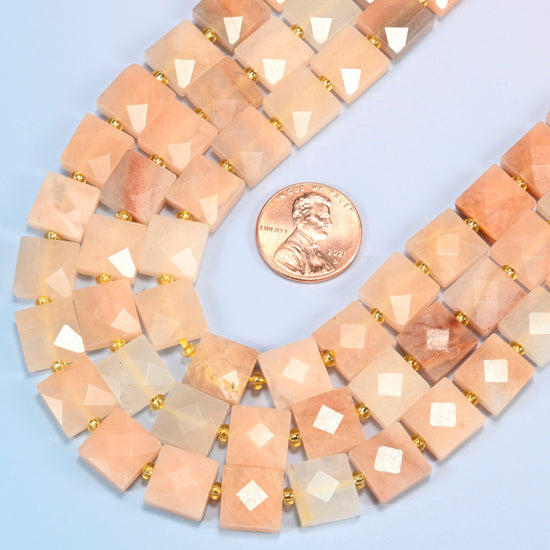 Close view of natural pink aventurine faceted flat square strands curving beside a US penny for scale