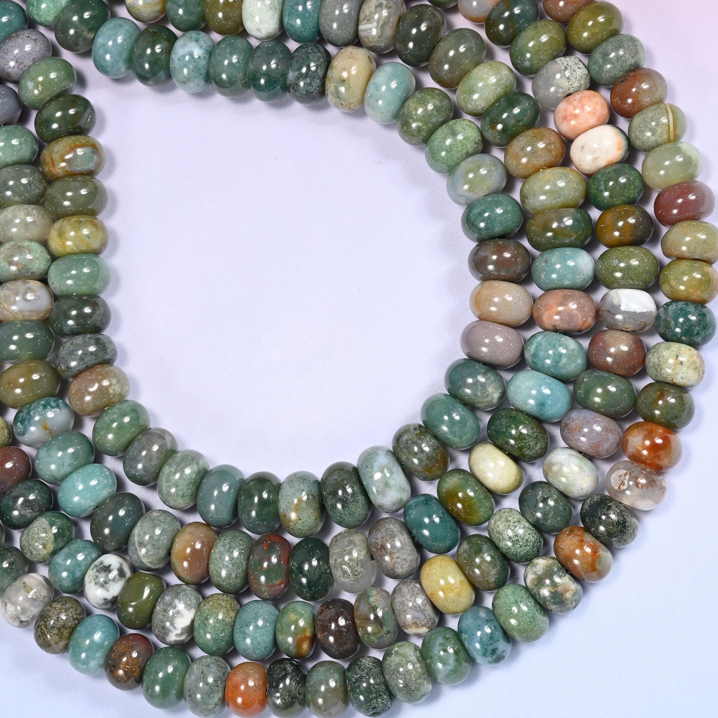 Circular coil of Indian Agate bead strands on a lavender background with a penny in the center for size comparison.
