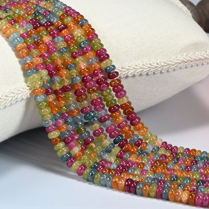 Tourmaline Color Dyed Jade smooth rondelle beads 3x6mm draped over a cream cushion, rose pink, warm orange, olive green and teal blue mixed bead to bead along every strand