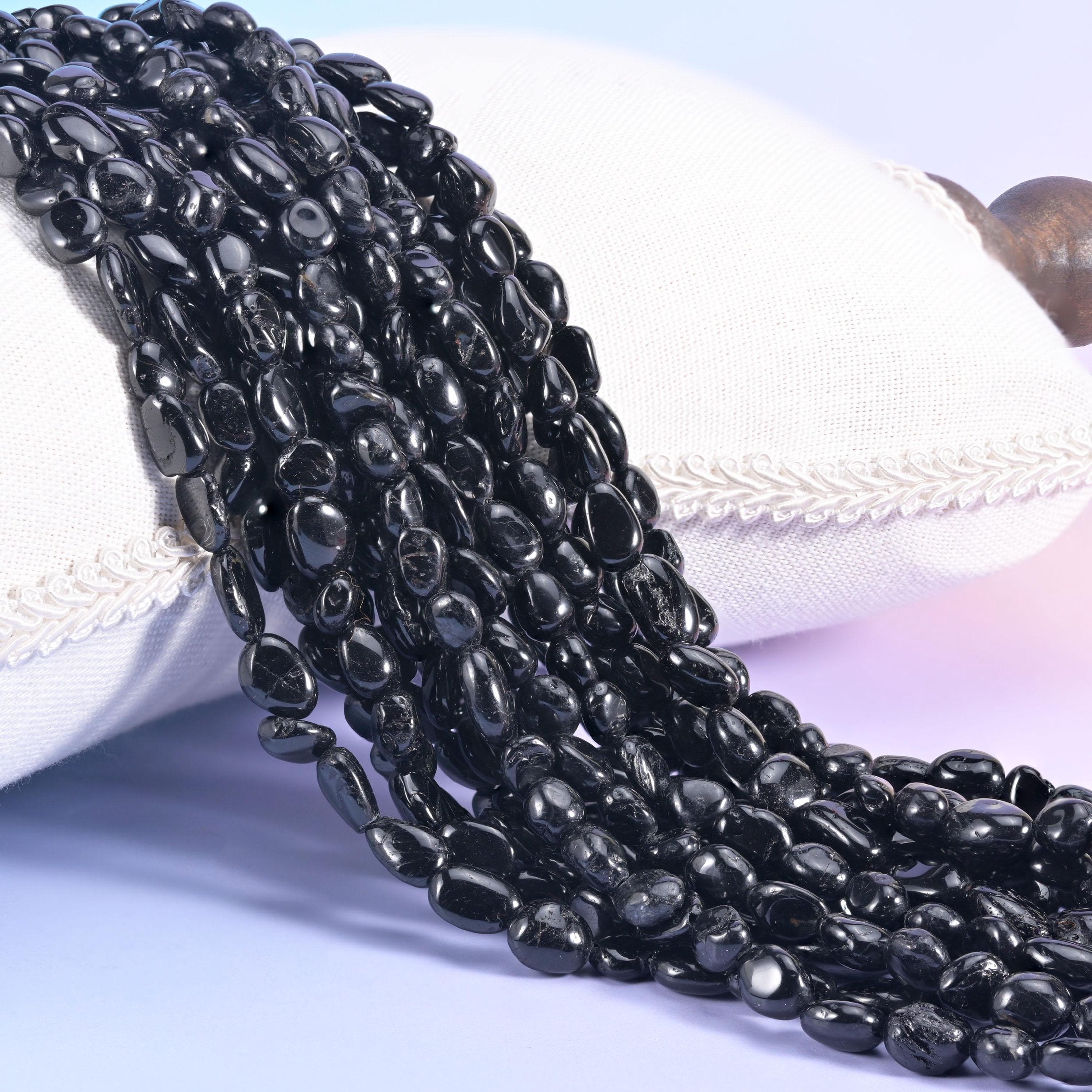 Jet black tourmaline nugget strands draped over a white cushion