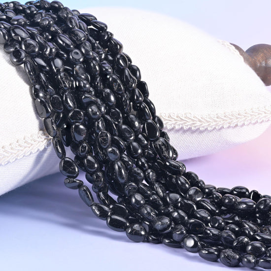 Jet black tourmaline nugget strands draped over a white cushion