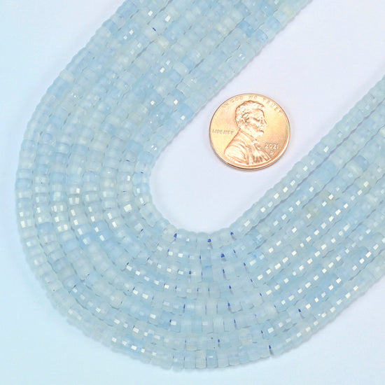 Close view of aquamarine chalcedony faceted heishi disc strands curving beside a US penny for scale
