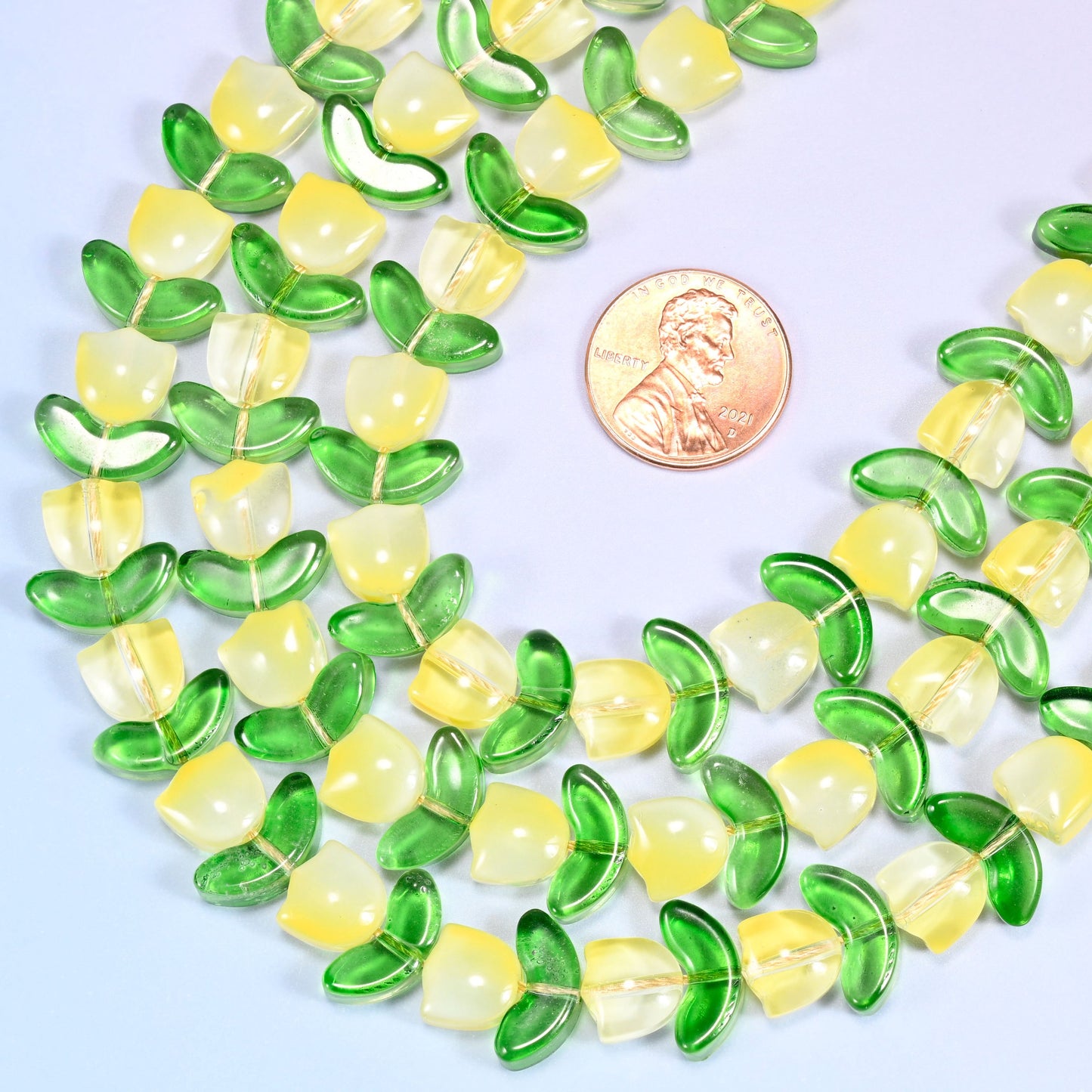 Wide view of a circular coil of yellow tulip and green leaf glass bead strands on a lavender and pink gradient background.