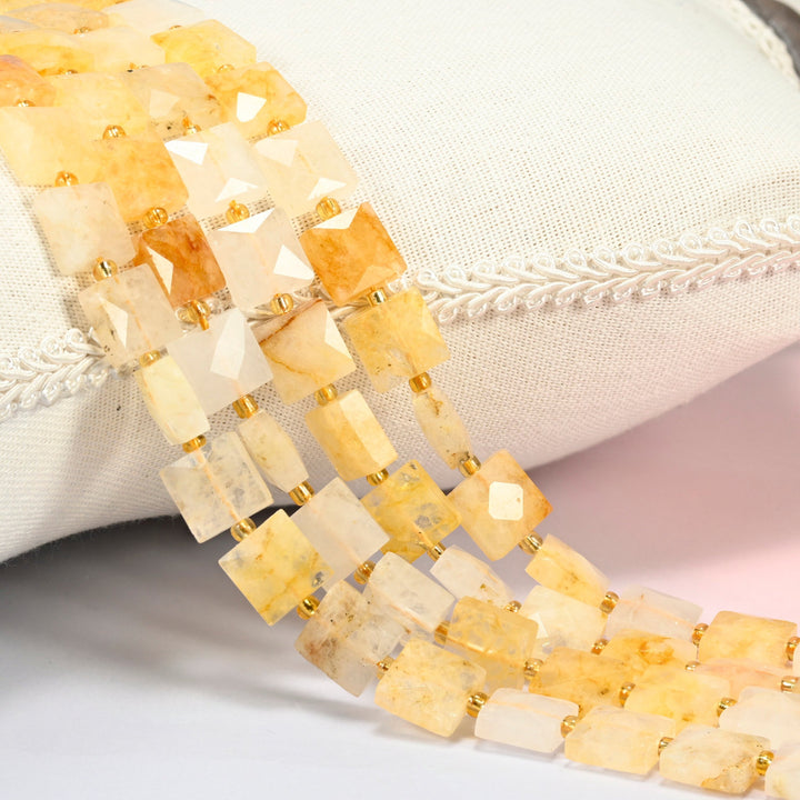 Natural golden healer quartz faceted flat square beads 10x10mm with small gold seed bead spacers, several strands draped over a white cushion