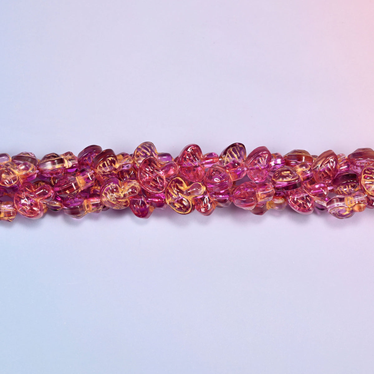 Pink gold flat mushroom glass beads, domed caps over short stems, strands laid in a gentle wave straight across the frame.