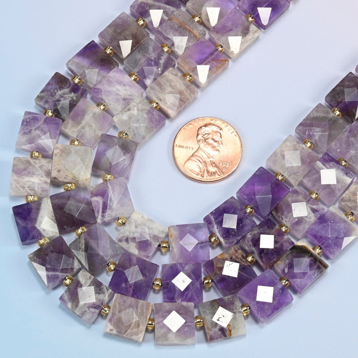 Close view of natural amethyst faceted flat square strands curving beside a US penny for scale