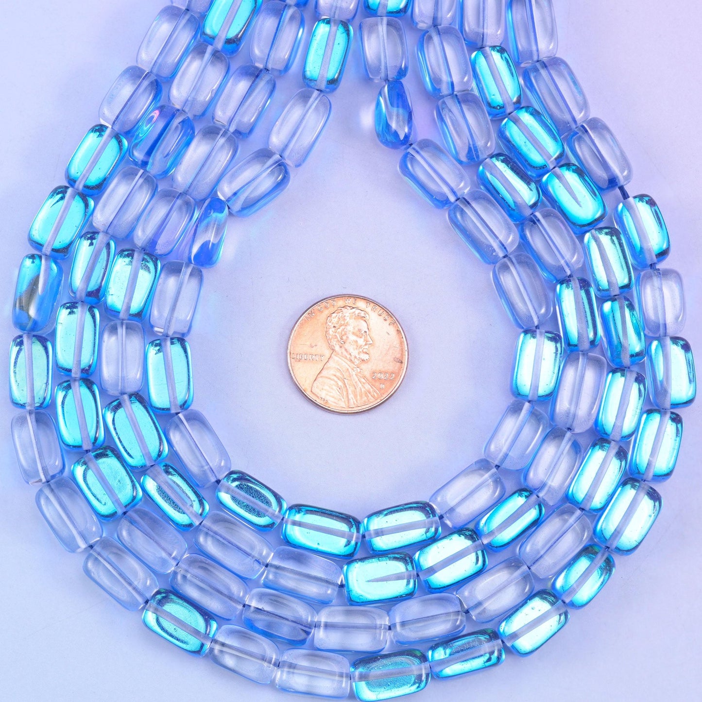 Sapphire blue rectangles in glossy transparent glass, coated in Mystic Aura so a soft iridescent film sits over the deep blue. Cut flat on every side and drilled through the length for easy stringing.