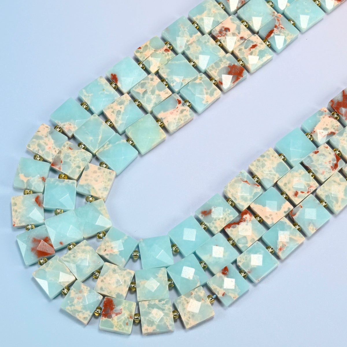 Dyed blue Shoushan stone faceted flat square beads in several strands curved into a wide U, light blue stone with cream and red-brown matrix