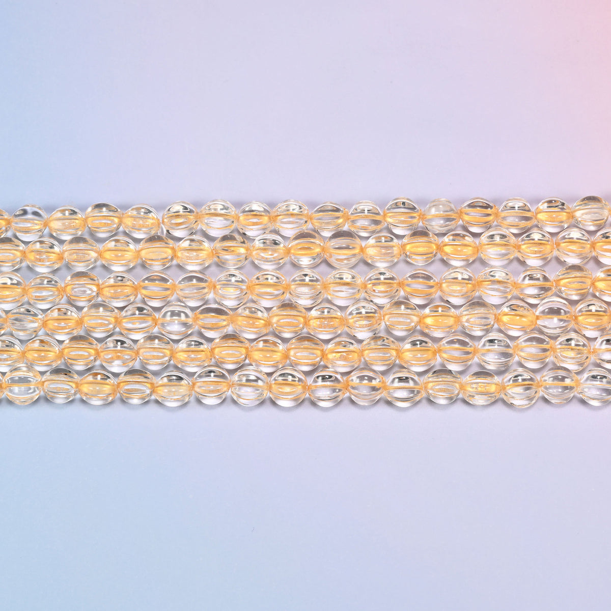 Close-up of 8mm clear gold pumpkin glass beads in four horizontal rows, showing the carved melon ribs.