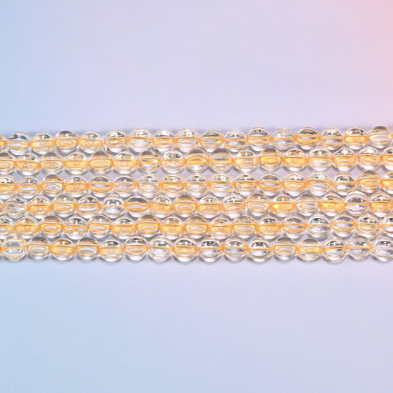 Close-up of 8mm clear gold pumpkin glass beads in four horizontal rows, showing the carved melon ribs.