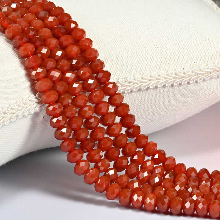 Red agate faceted rondelle beads in deep brick red and warm orange-red, three strands draped over a linen cushion