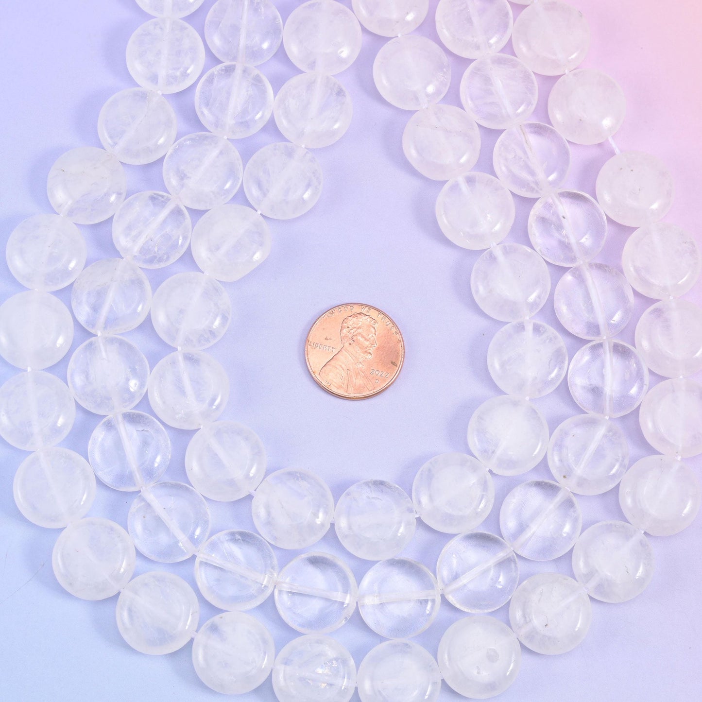 Overhead loop of quartz coin beads around a penny on a pink-lilac gradient