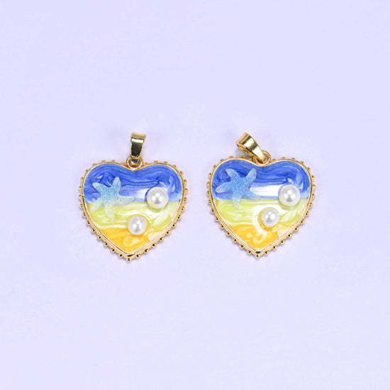 Enamel Heart Pendants in blue, two charms photographed close together so the blue wave, yellow sand and pearl accents are clear.
