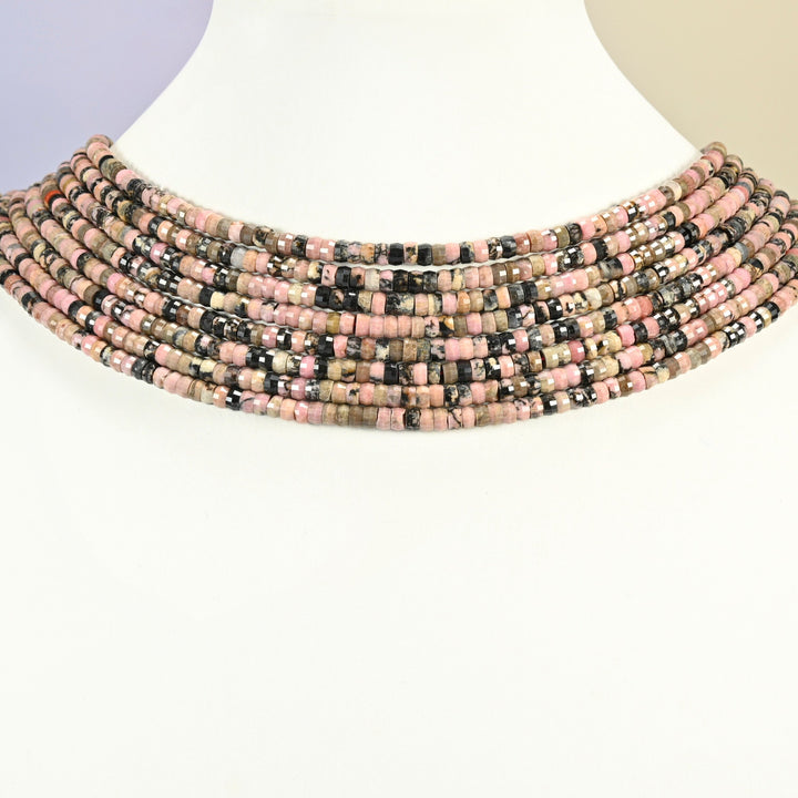 Rhodonite faceted heishi disc strands arranged as a layered collar on a white display bust, pink and black beads across the neck