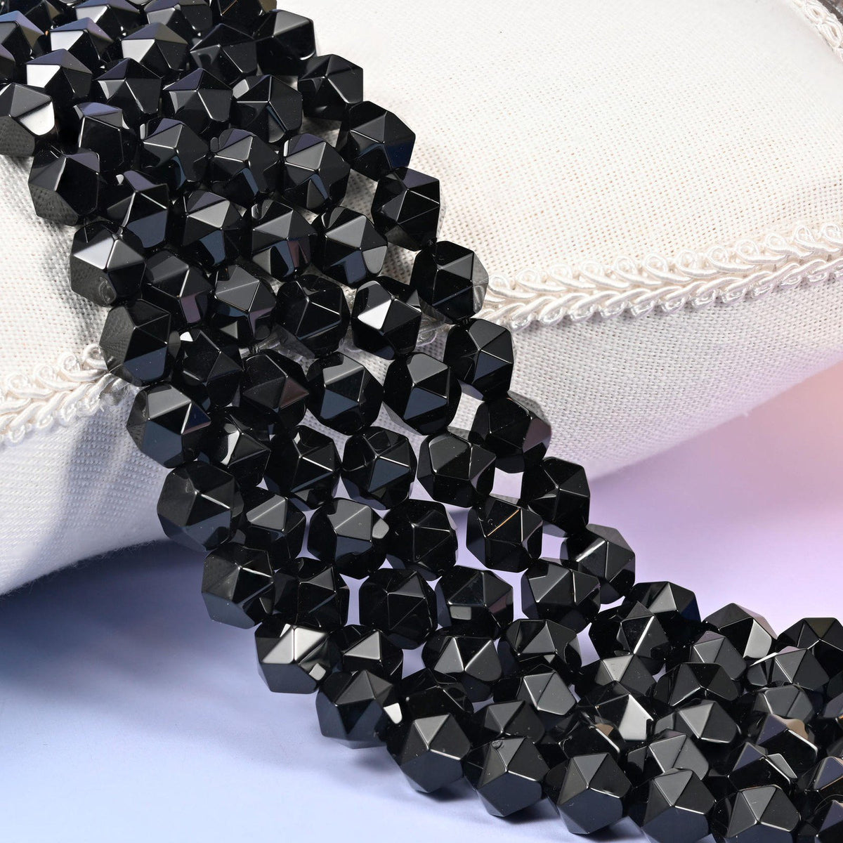 Black Onyx diamond star cut beads, strands laid over white fabric, glossy solid black with sharp facet edges