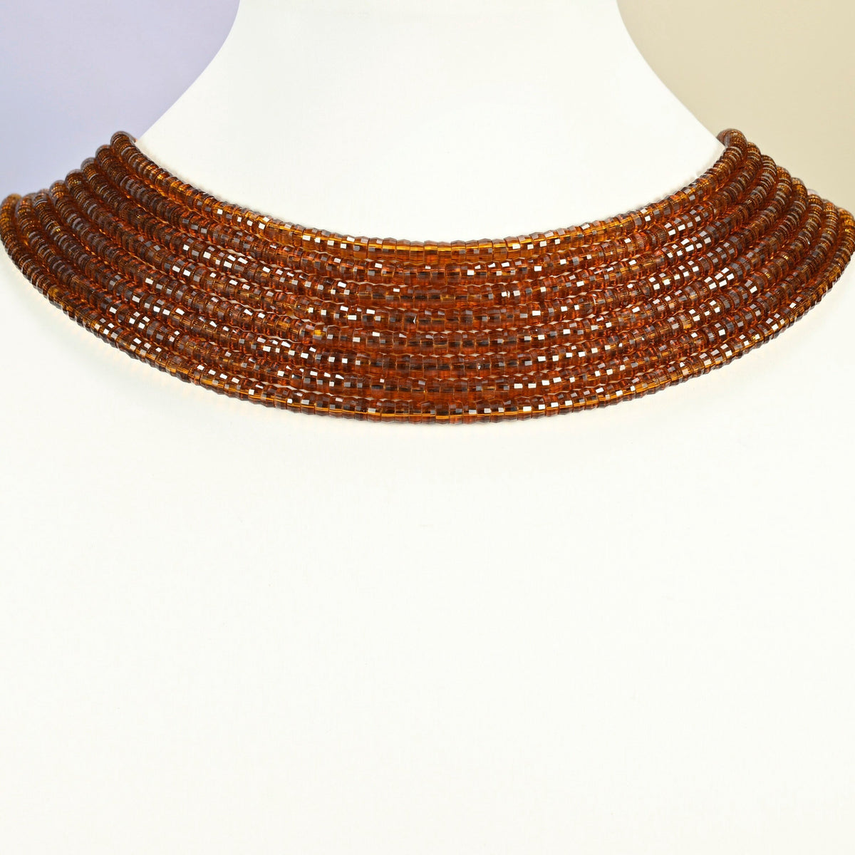 Brown glass faceted heishi disc strands arranged as a layered collar on a white display bust, amber brown beads across the neck
