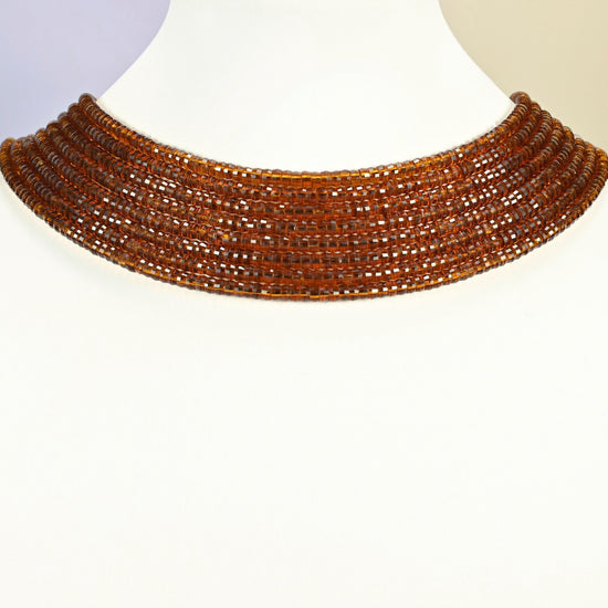 Brown glass faceted heishi disc strands arranged as a layered collar on a white display bust, amber brown beads across the neck