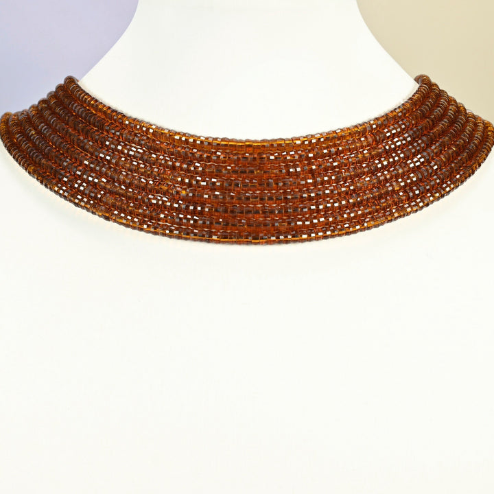 Brown glass faceted heishi disc strands arranged as a layered collar on a white display bust, amber brown beads across the neck