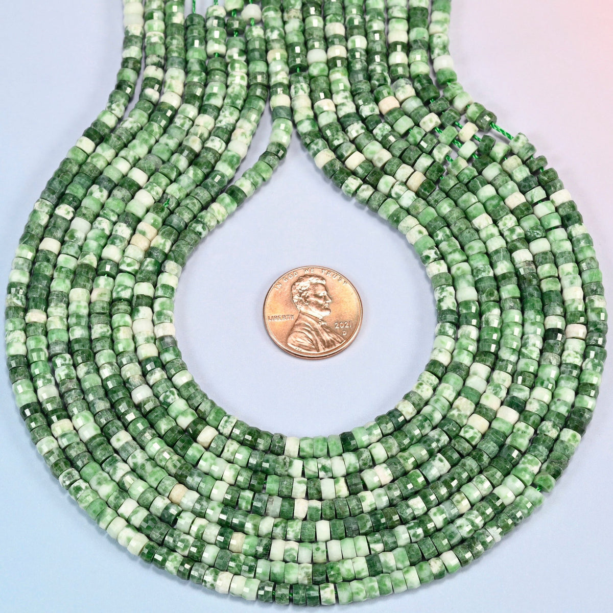 Tree agate faceted heishi disc strands formed into a teardrop loop around a US penny for scale