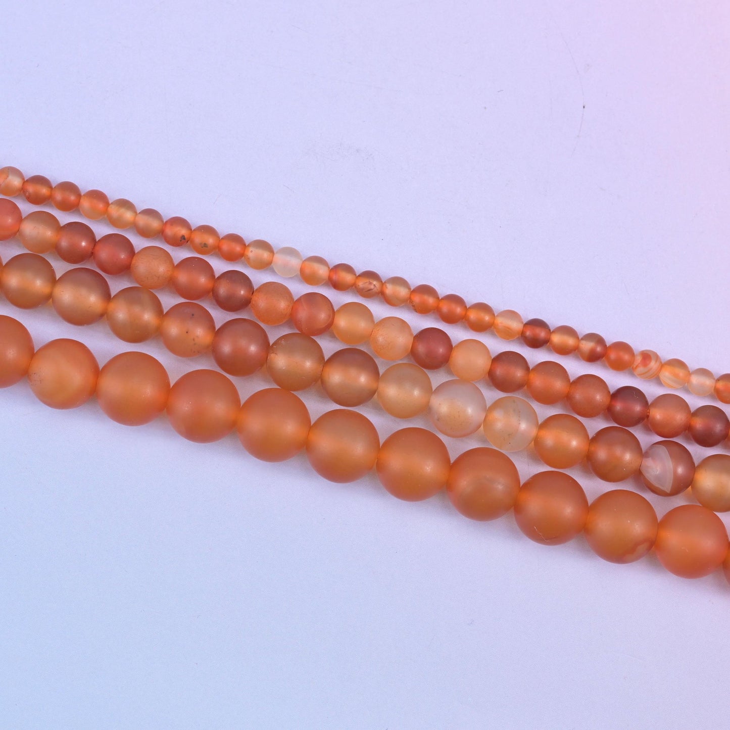 Orange Carnelian beads, some glowing amber and others pale and creamy where the stone turns translucent
