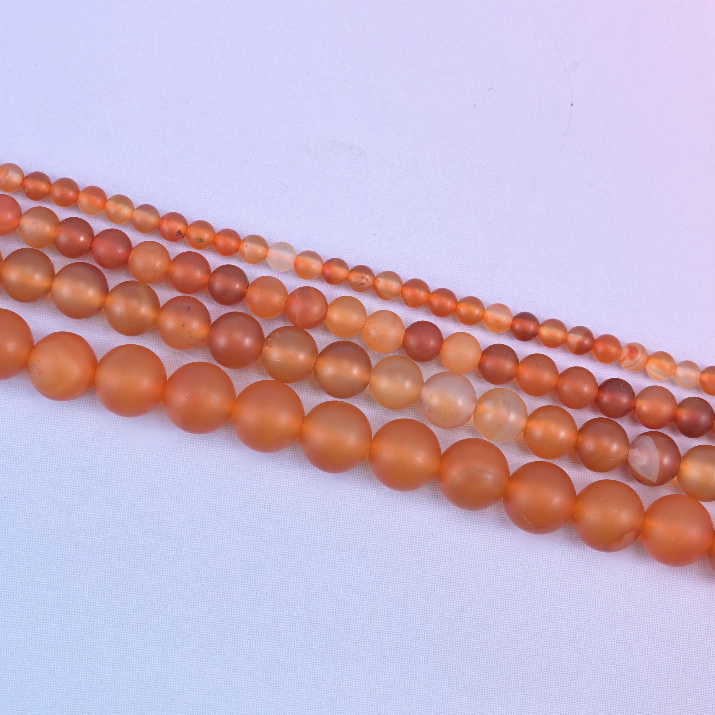 Orange Carnelian beads, some glowing amber and others pale and creamy where the stone turns translucent
