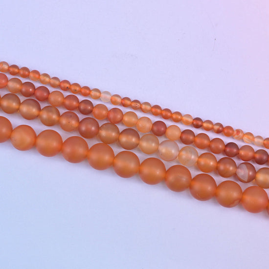 Orange Carnelian beads, some glowing amber and others pale and creamy where the stone turns translucent