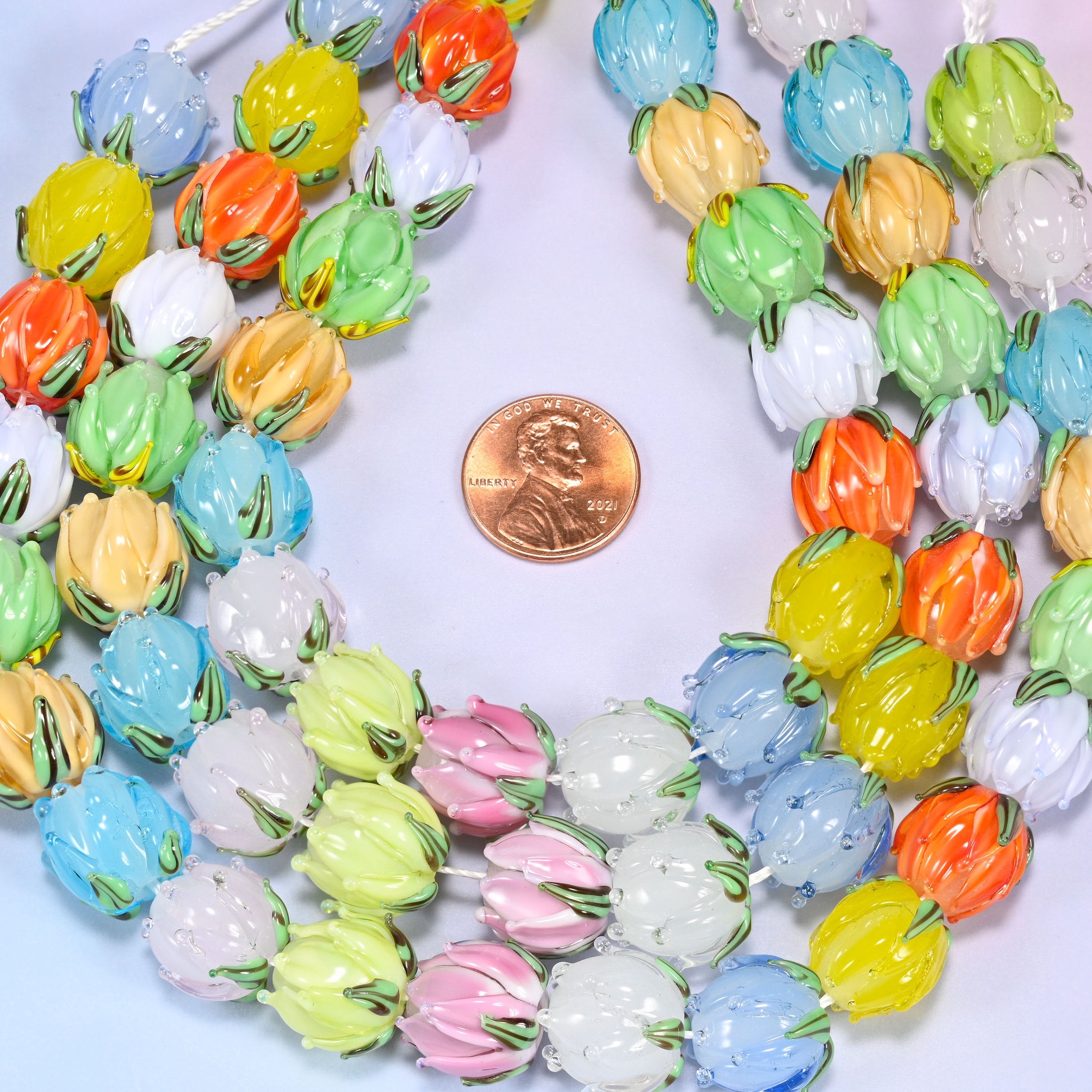 Circular coil of tulip bud lampwork glass bead strands on a lavender background with a penny in the center for size comparison.