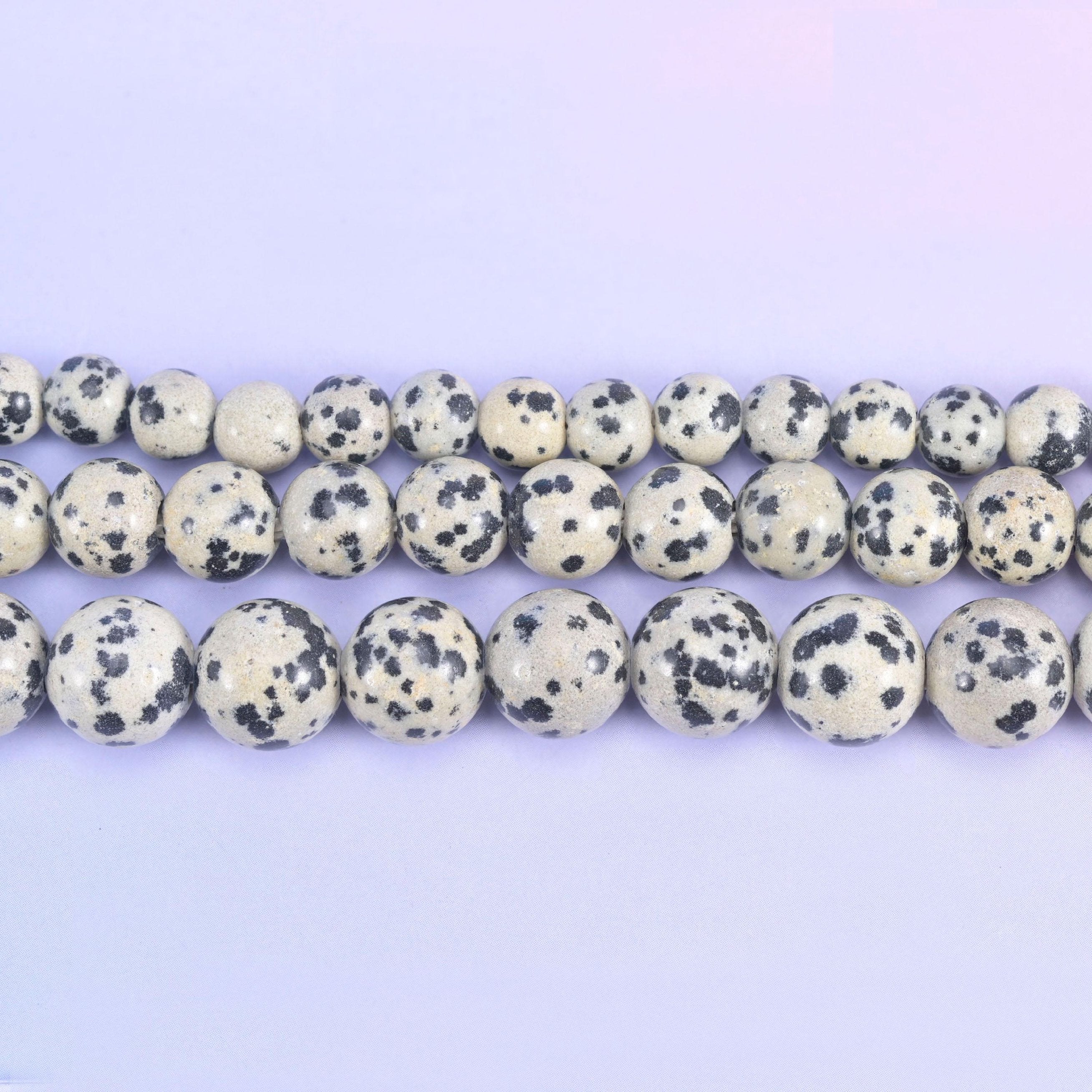 Cream and bone-white rounds scattered with inky black spots, exactly the marking the name promises, polished smooth and drilled 2.0-2.5mm so leather, hemp and heavy cord thread straight through.