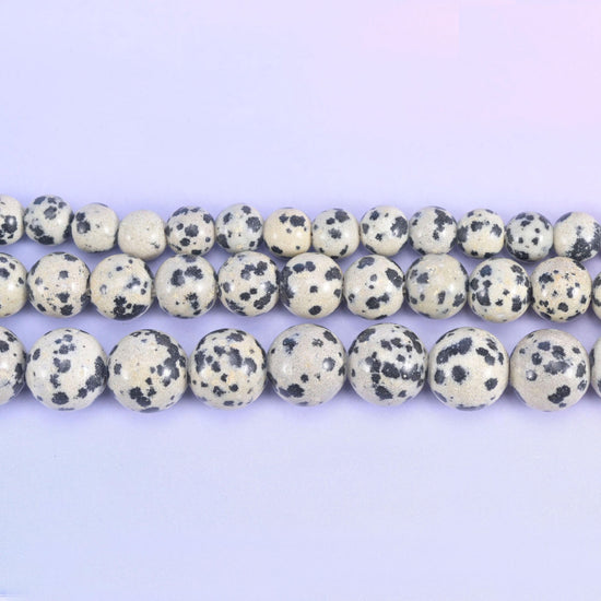 Cream and bone-white rounds scattered with inky black spots, exactly the marking the name promises, polished smooth and drilled 2.0-2.5mm so leather, hemp and heavy cord thread straight through.