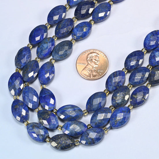 Close view of lapis lazuli faceted flat oval strands curving beside a US penny for scale