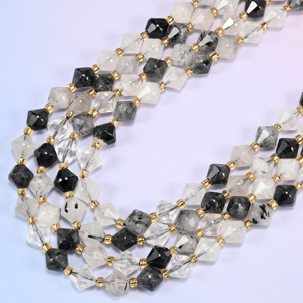 Black rutilated quartz bicone beads in a wide loop curving down and back, needle density varying bead to bead, from a faint scatter to dense black.