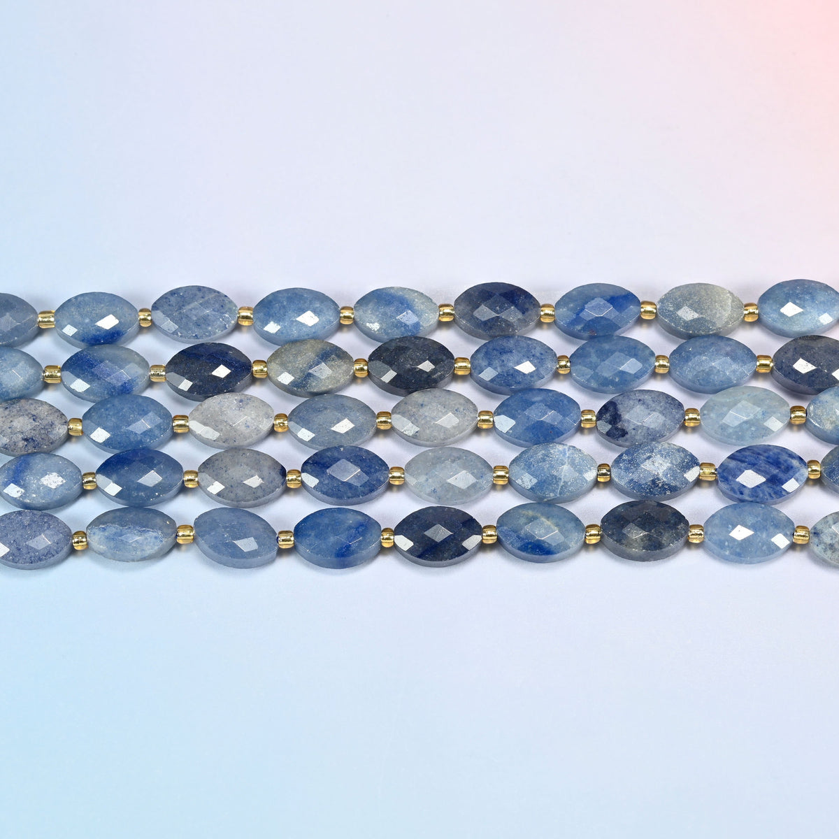 Several strands of blue aventurine faceted flat oval beads laid in straight rows with gold seed bead spacers