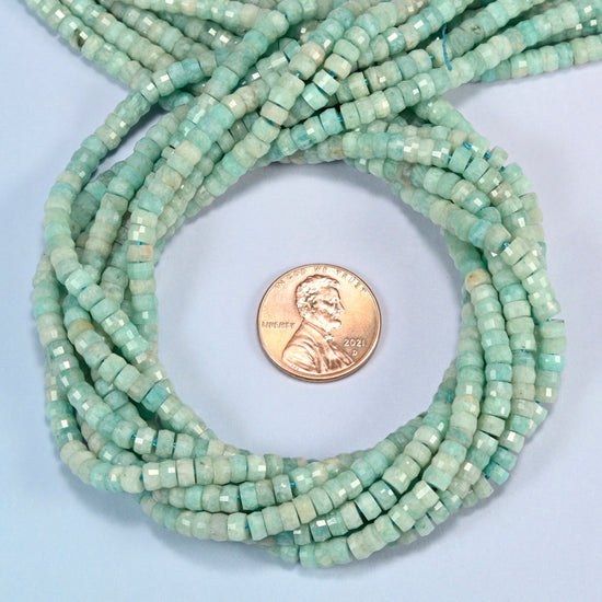 Green amazonite faceted heishi disc beads 2x4mm coiled in a loop around a US penny for scale, close-up of the faceted disc shape